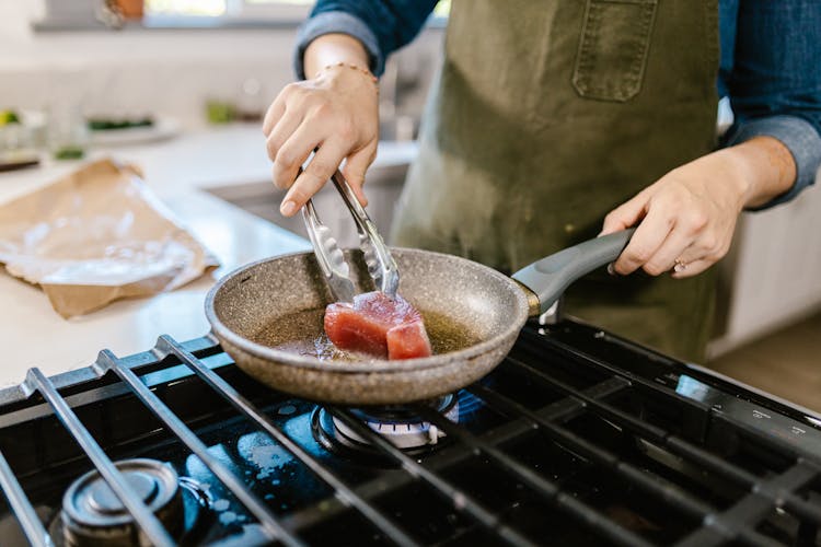 Female Hands Holding Frying Pan And Putting Chunk Of Meat In Hot Frying Oil