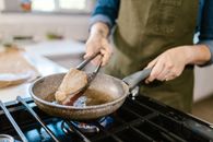 Chunk of Tuna Fish Meat Turned on Frying Pan by Kitchen Pincers in Chefs Hand