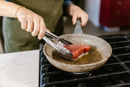 Close-up of a person frying a fresh tuna steak in a pan on a gas stove.