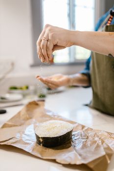 A cook sprinkles seasoning on a fish slice, preparing a meal in a bright kitchen.