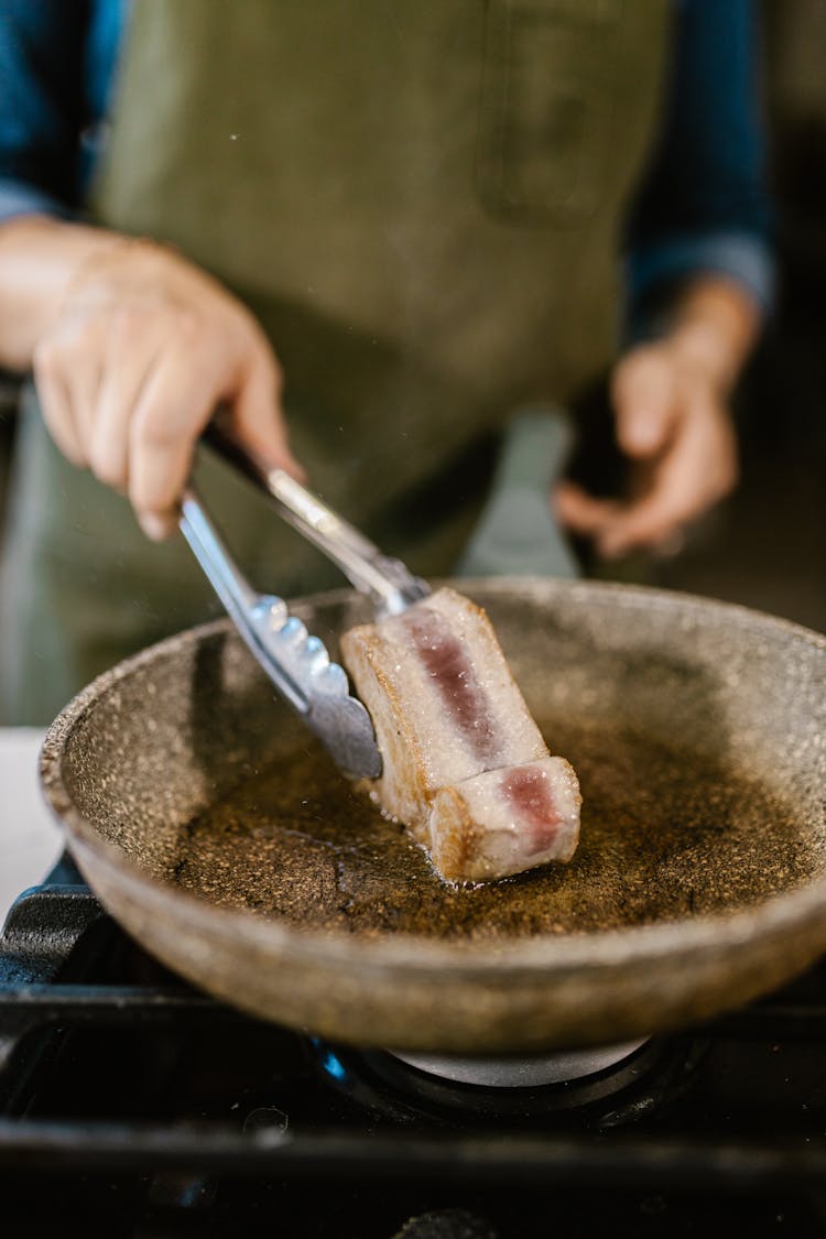 Unrecognizable Chefs Hand Turning Fish Slice On Frying Pan With Kitchen Pincers