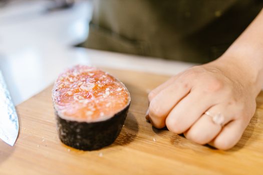 A close-up view of a fresh salmon fillet next to a hand on a cutting board.