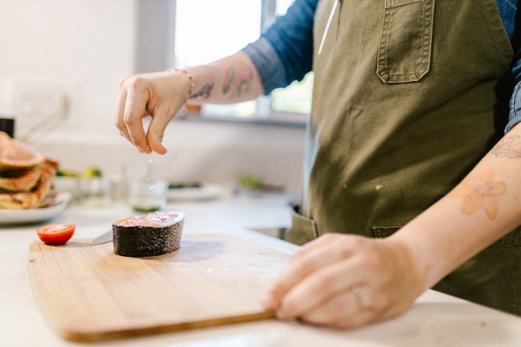 Unrecognizable Female Hand Sprinkling Salt On Fish Slice