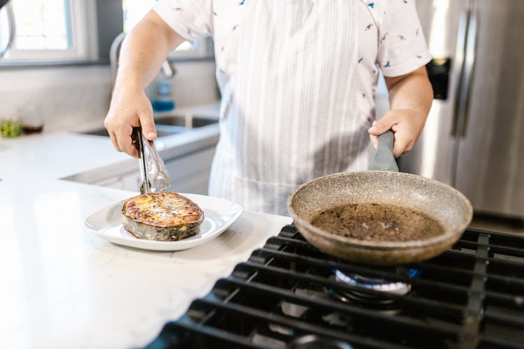 Cook Putting Portion Of Ready Fried Salmon Slice On Plate