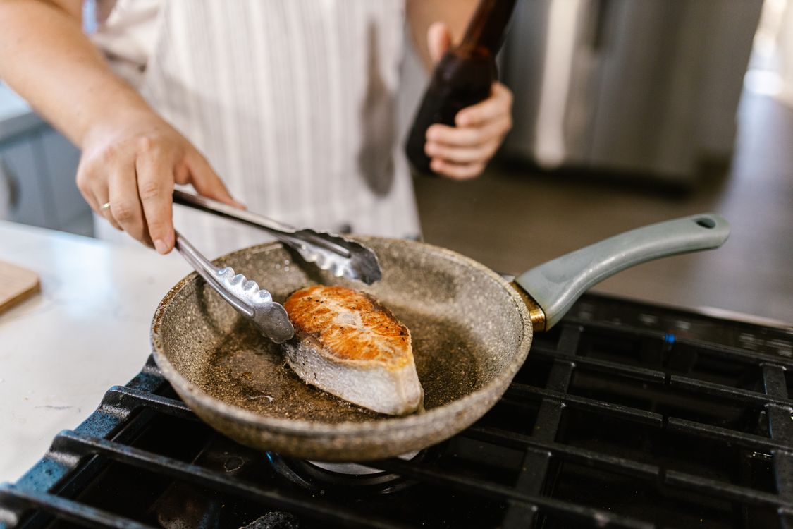 Salmon fillet cooking in a speckled non-stick frying pan on a gas stove
