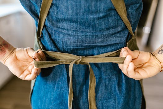 A woman ties an apron in a cozy kitchen setting, focusing on hands and fabric.
