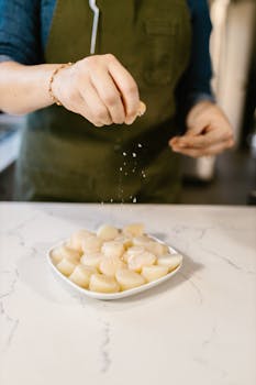 Close-up of unrecognizable person sprinkling salt on fresh scallops indoors.