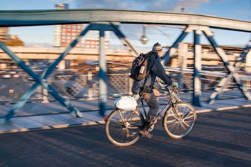 패닝 사진에서 회색 콘크리트 도로에서 검은 자전거를 타고 검은 재킷을 입은 남자