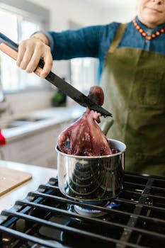 A chef is cooking octopus using tongs over a stove in a modern kitchen setting.