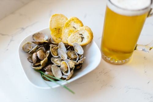 Free Delicious seafood clams paired with crunchy bread and a mug of beer on a white surface. Stock Photo