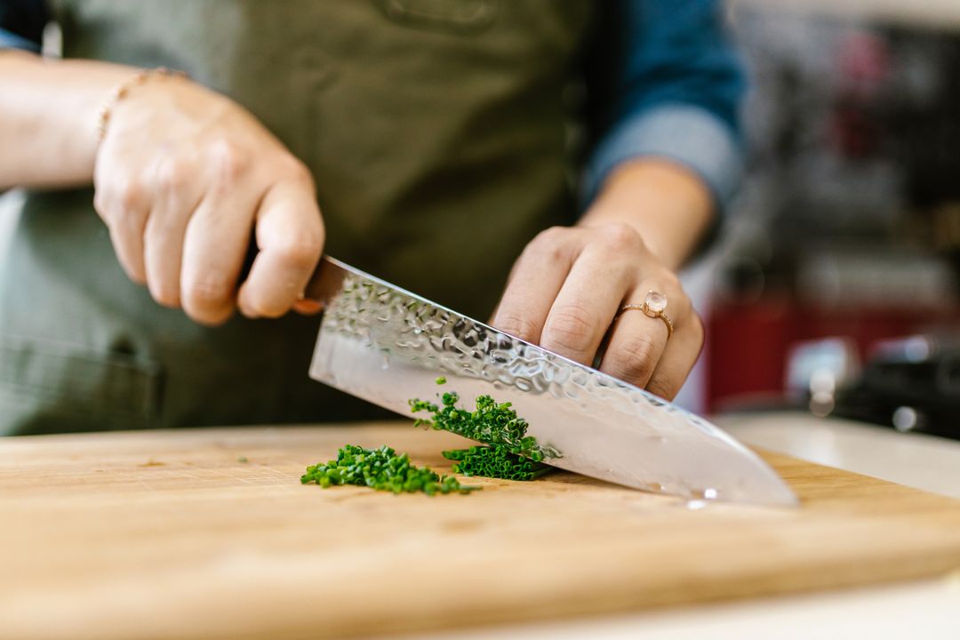 10 Essential Knife Skills Every Home Cook Must Learn 2 Close-up of hands using the pinch grip and claw technique while mincing fresh herbs on a wooden cutting board.