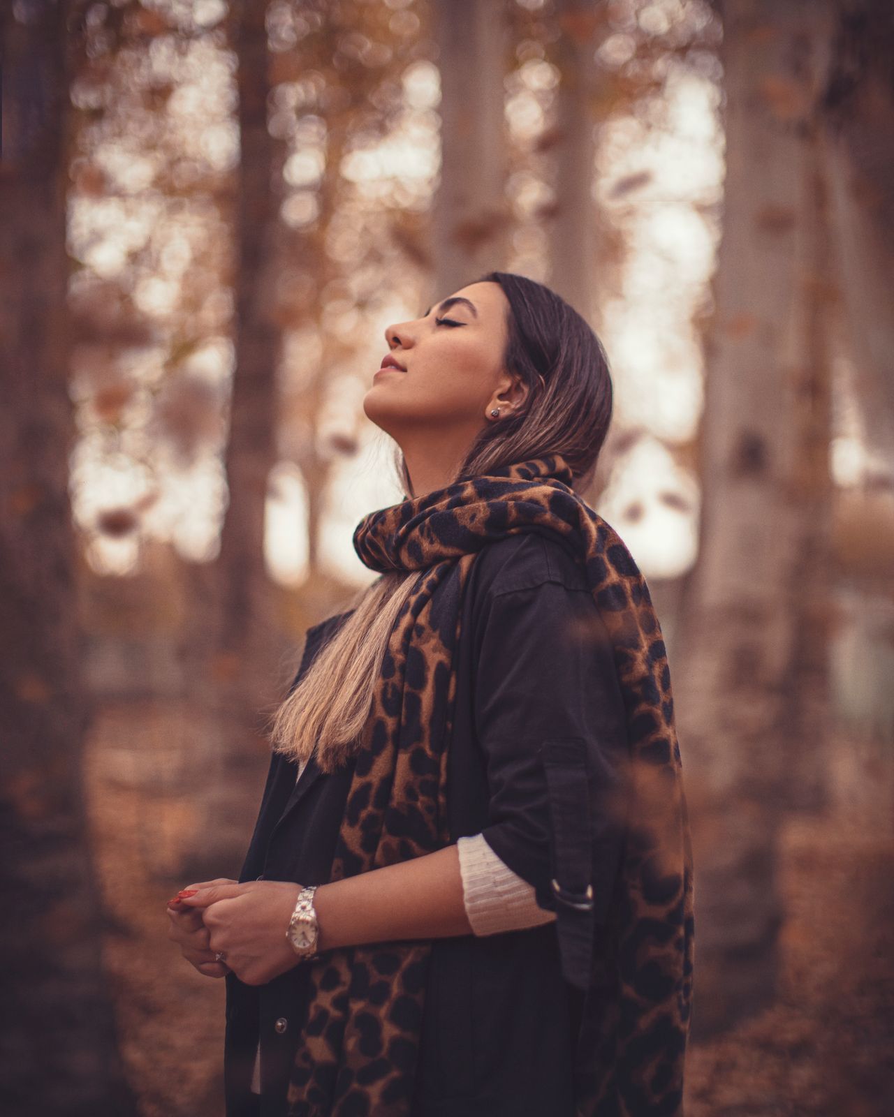 Woman wearing a leopard-print scarf with a black top in autumn woods