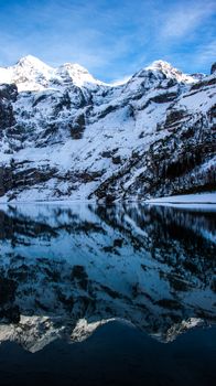 Snowy mountains reflected in a calm alpine lake in Kandersteg, creating a serene winter scene.