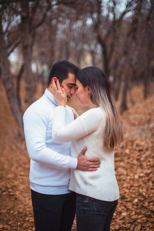 Free A loving couple in white sweaters embracing tenderly in an autumn forest setting with fallen leaves. Stock Photo