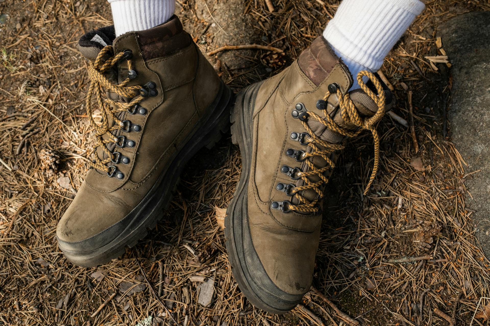 Brown hiking boots with socks on a forest path in a close-up view.