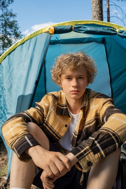 Free Young teenager with curly blonde hair sitting in a camping tent during summer Stock Photo
