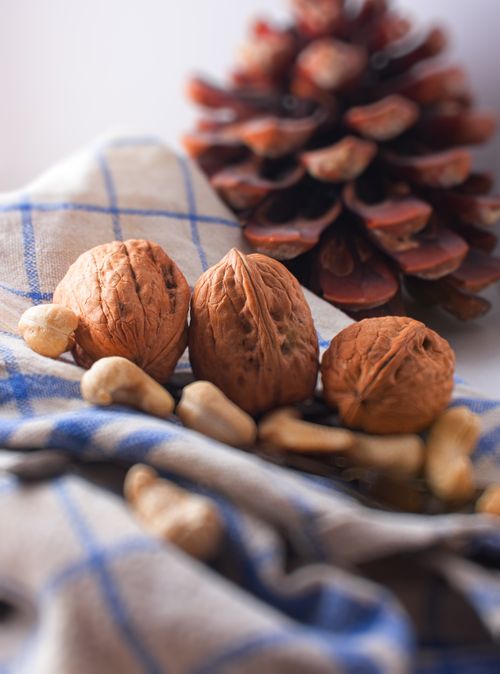 Free A close-up of walnuts and cashews on a checkered cloth with a pine cone. Stock Photo