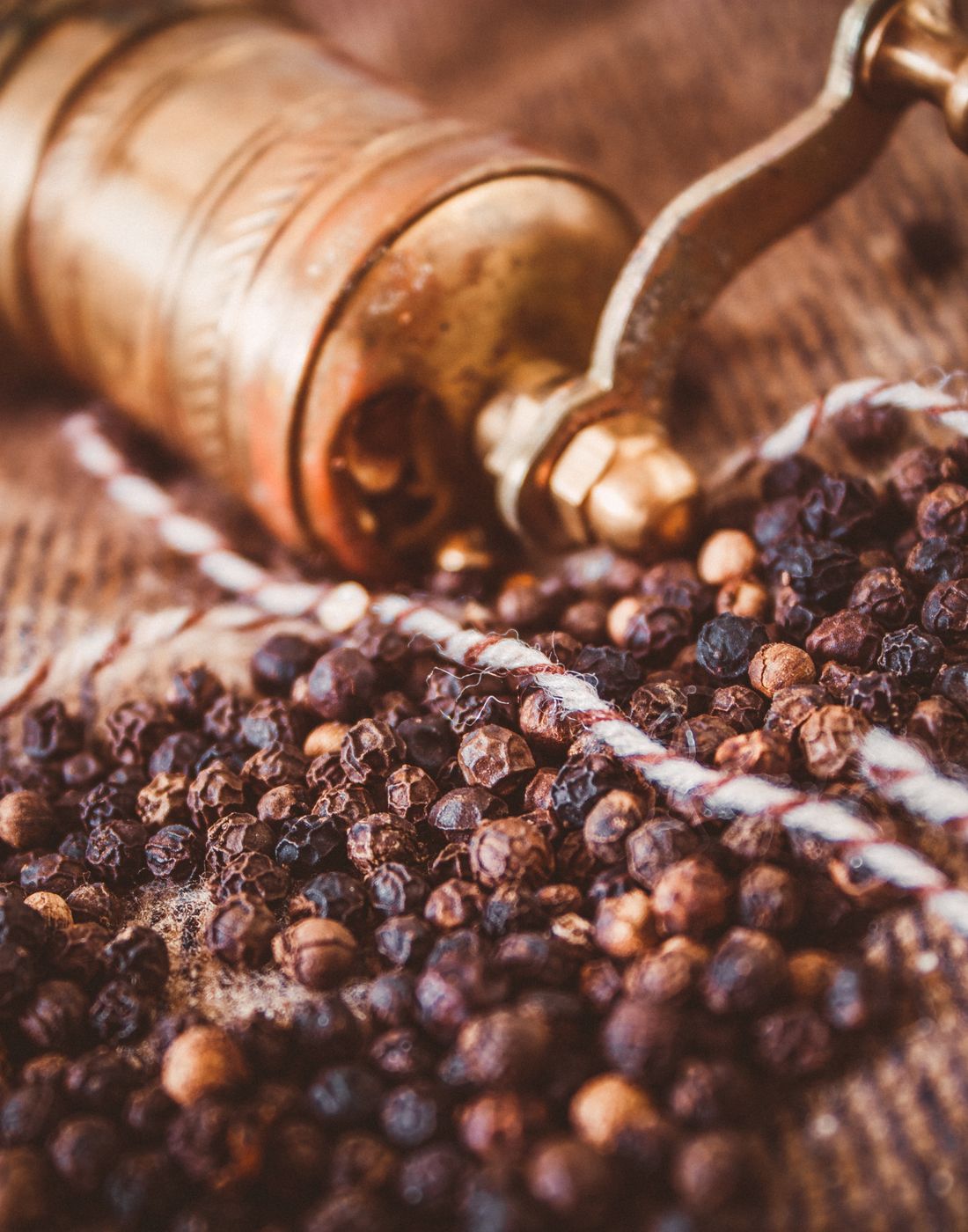 Black peppercorns beside a brass grinder