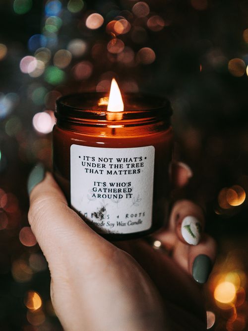 Free Hand holding a lit candle with festive multicolored lights in the background, creating a warm holiday atmosphere. Stock Photo