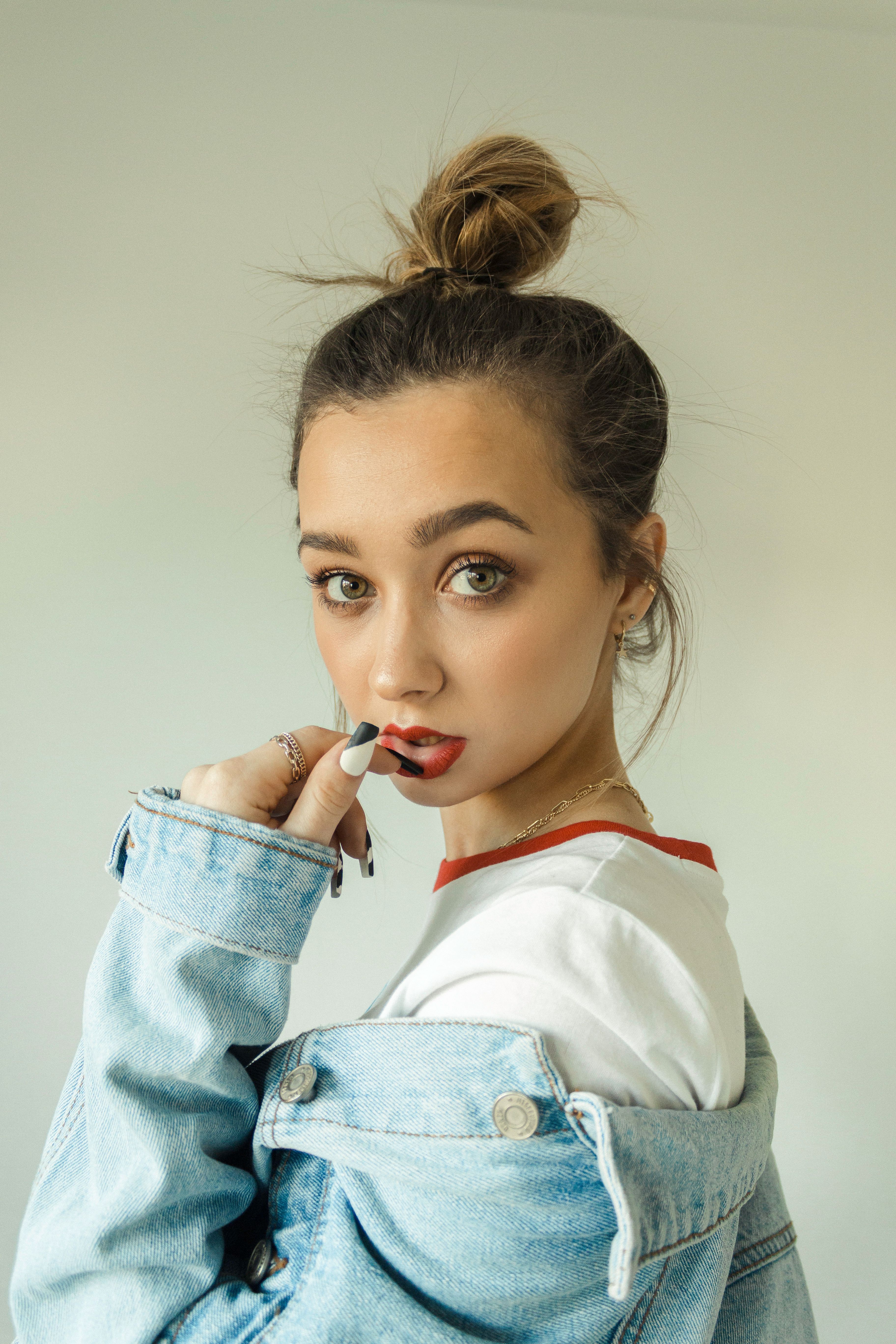 A trendy young woman poses in a denim jacket with a stylish top knot.