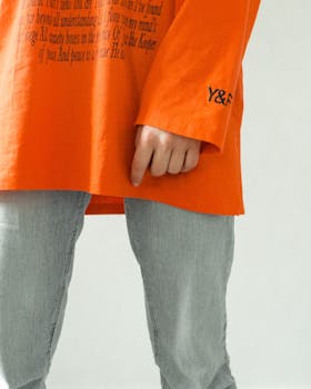 Detailed view of a person wearing an orange sweater and denim pants, showcasing casual fashion.