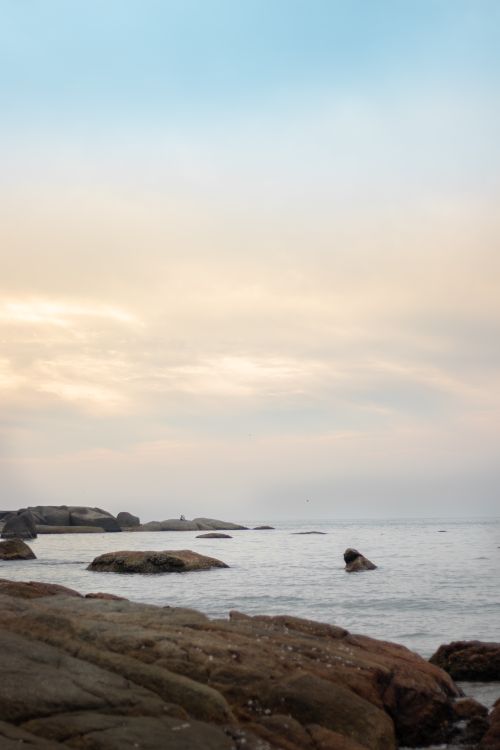 Free A serene view of a rocky shoreline under a cloudy sky at sunset. Ideal for nature themes. Stock Photo