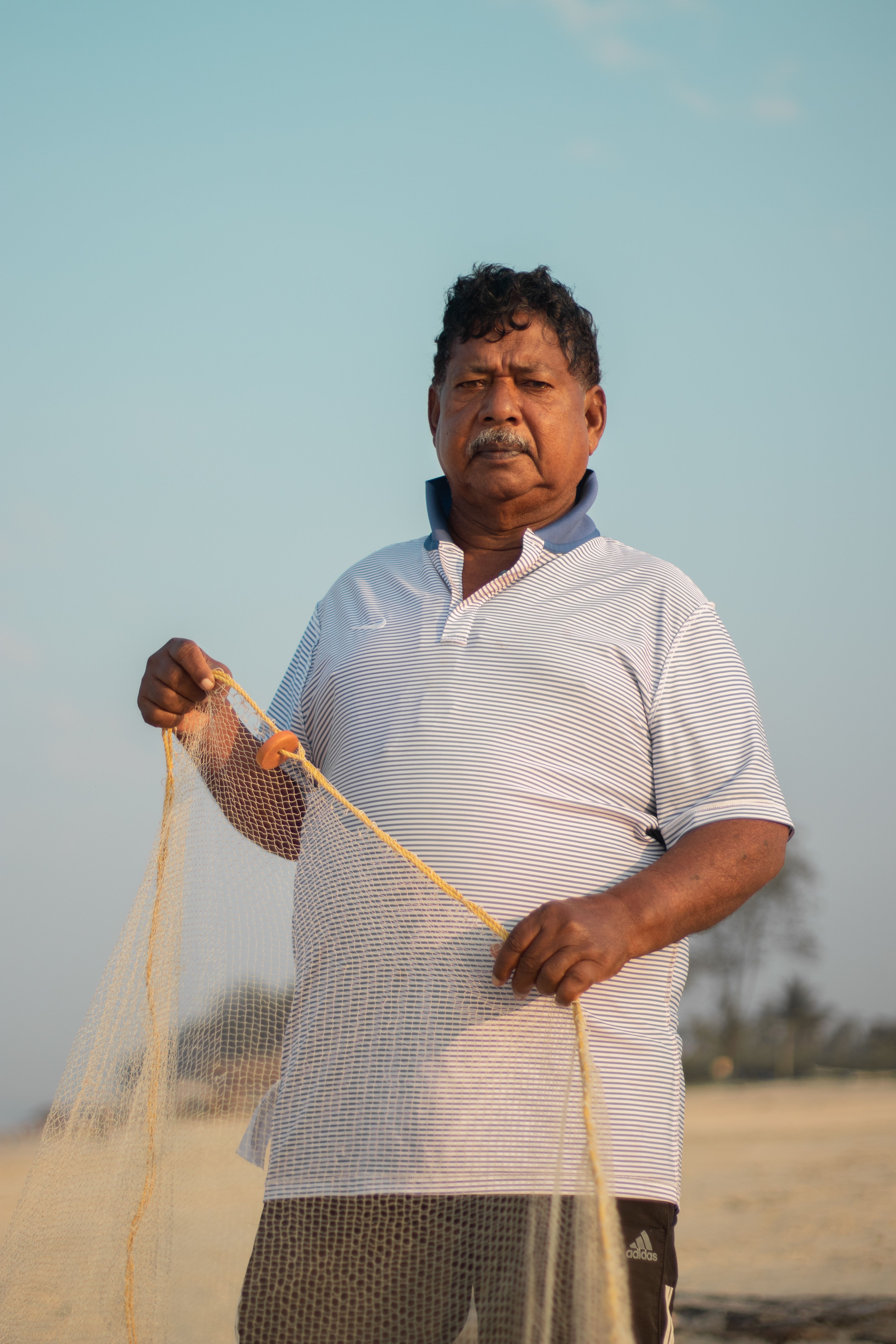 Fisherman holding a net on a sunny beach, wearing a striped polo shirt, ready for a catch.