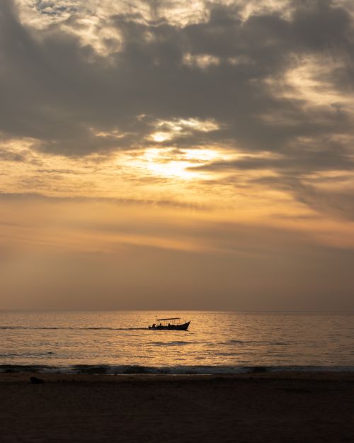 Free A silhouette of a boat on the ocean against a vibrant sunset sky. Perfect for travel and nature themes. Stock Photo