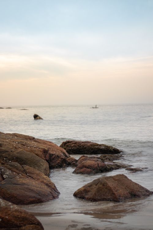 Free Peaceful evening seascape with rocks along the coast and calm waters under a pastel sky. Stock Photo