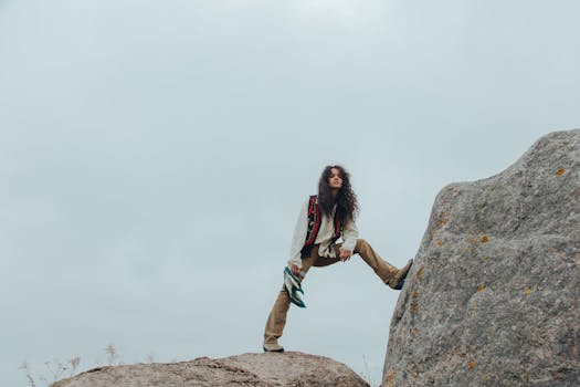 Woman with long hair climbing a large rock outdoors, wearing casual attire.