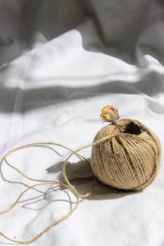 Close-up of hemp rope with a dried yellow flower on white fabric, emphasizing texture and light play.