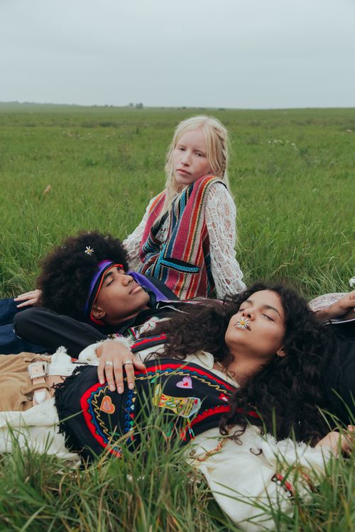 Free Three friends resting in a grassy field, showcasing bohemian fashion and diverse cultural representation. Stock Photo
