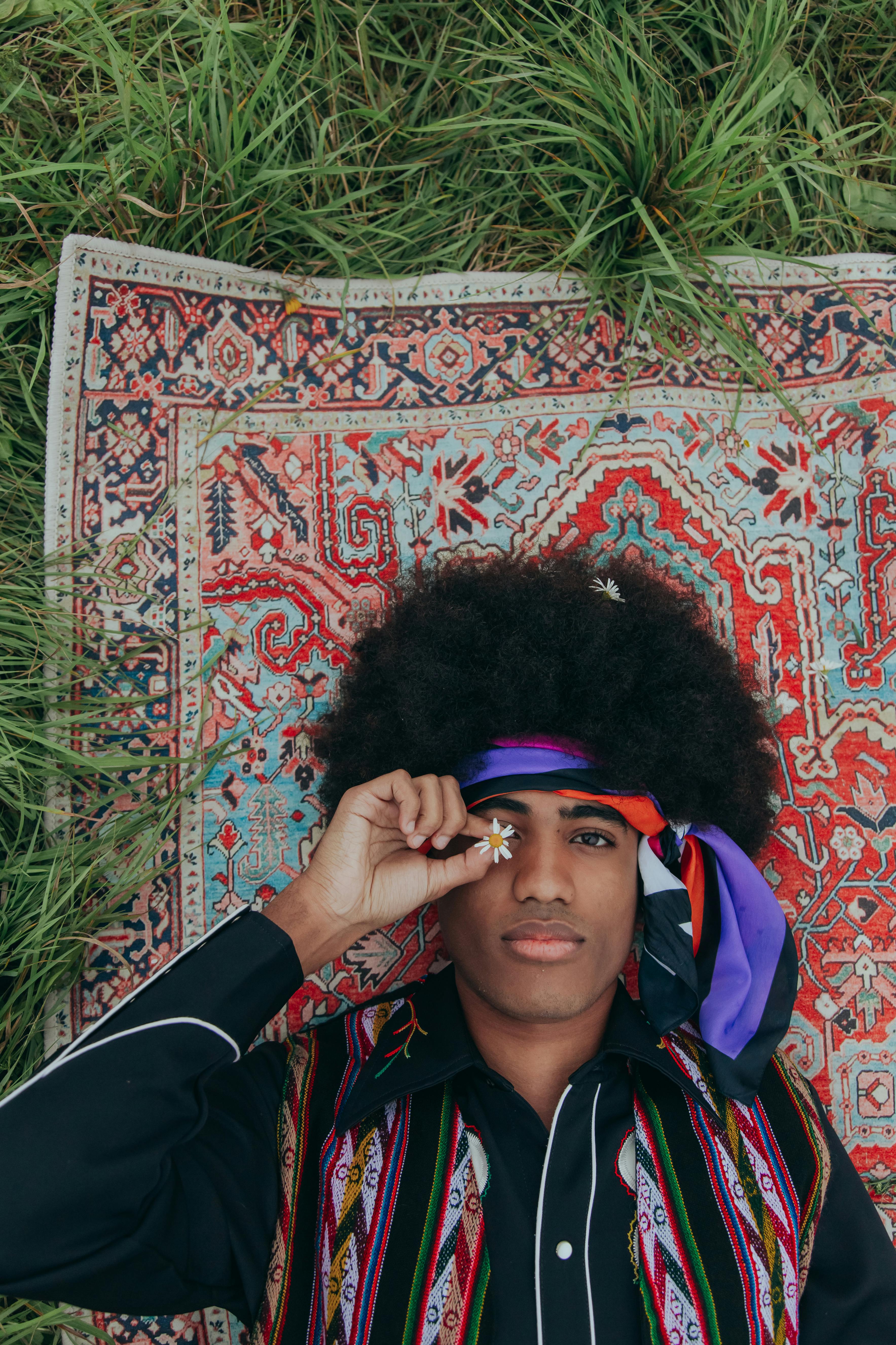 Young man with afro hair lying on a vibrant patterned rug in a serene outdoor setting.