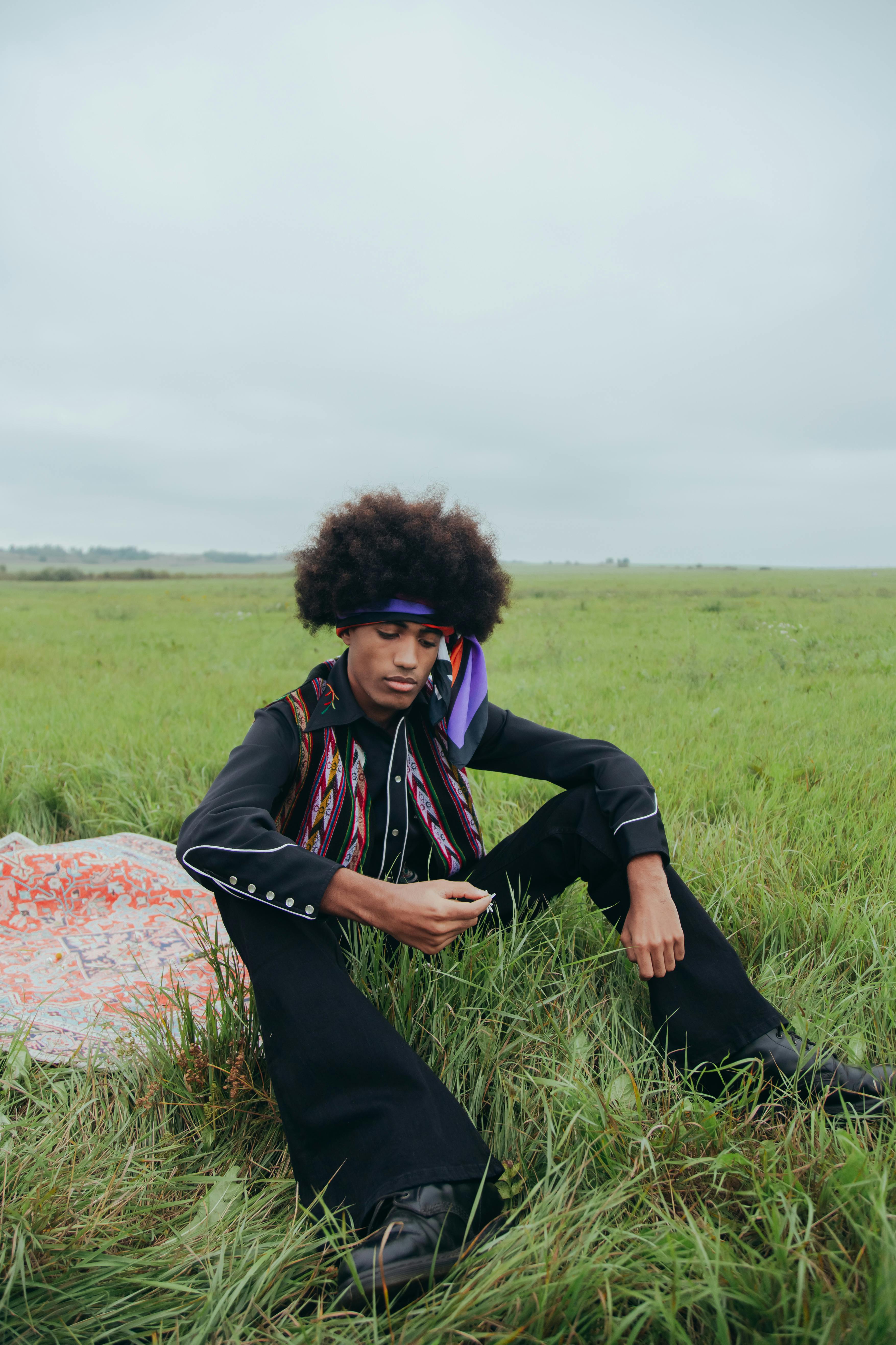 Young man with afro hair in hippie style sitting outdoors in a grass field