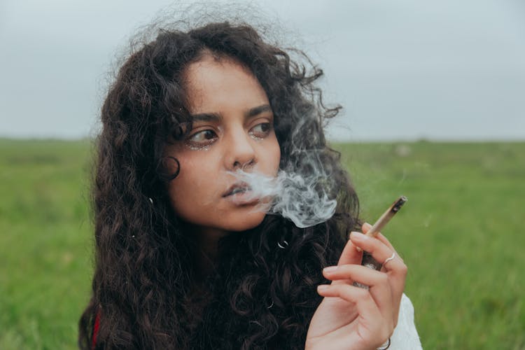 A Woman With Curly Hair Smoking While Looking Afar