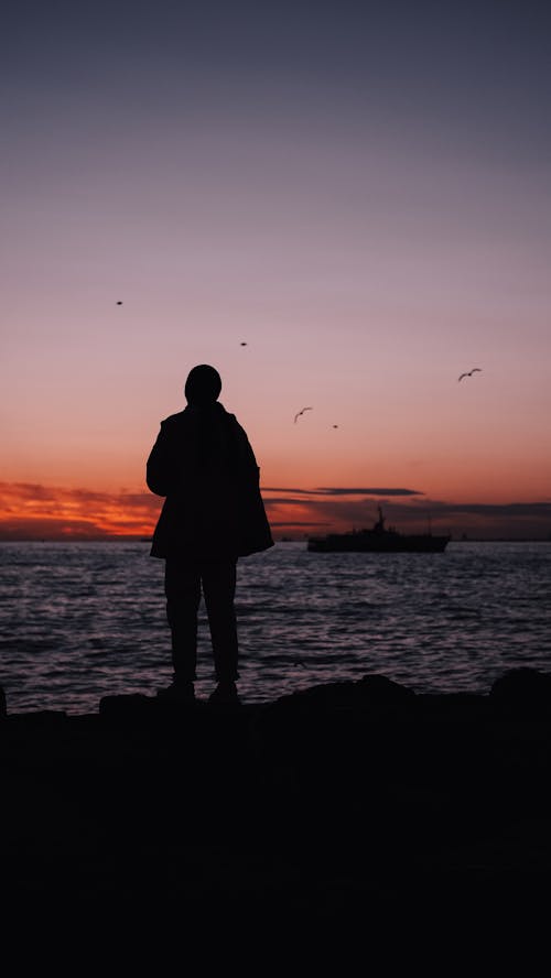 Silhouette of a Person near the Sea during Sunset