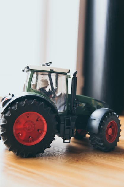 Black and Green Farm Tractor Toy on Brown Wooden Table Beside Window