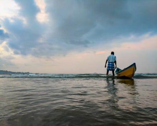 Man on Body of Water Beside Yellow and Blue Boat