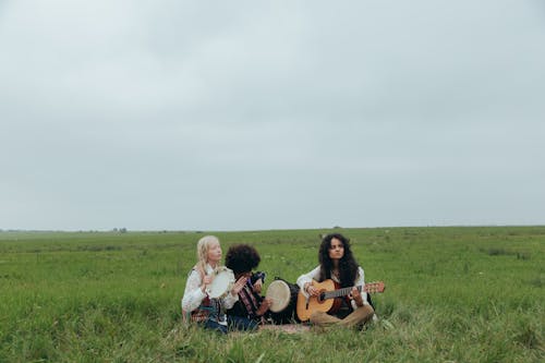 People Sitting on Grass Field while Playing Instruments