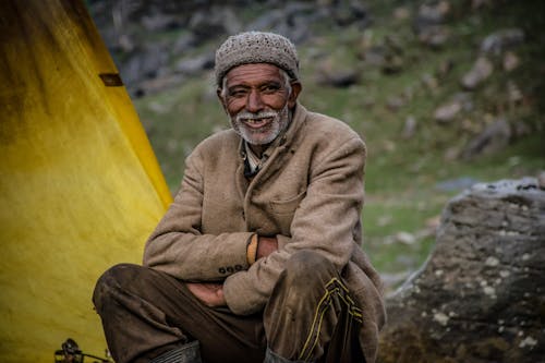 Uomo Sorridente Che Indossa Berretto In Maglia Grigio Seduto Vicino A Grey Rock