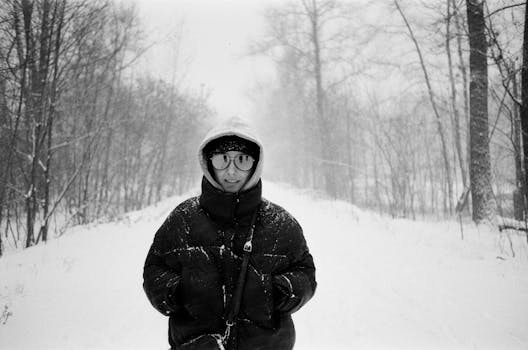 A person in warm clothing enjoys a snowy forest walk in black and white.