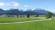 湛蓝的天空下，美丽的山区景观中，郁郁葱葱的绿色草地、森林覆盖的山丘和白雪皑皑的山峰尽收眼底