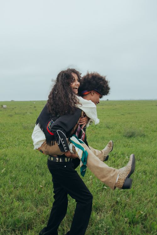Free Interracial couple having fun with a piggyback ride in a lush green field, capturing carefree joy and happiness. Stock Photo