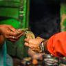 A close-up of two people exchanging Indian currency by hand at a vibrant outdoor market.