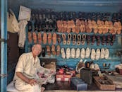 老人在传统鞋摊上读报纸，凉鞋挂在架子上