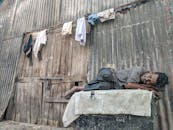 一位老人安详地躺在破旧的木墙上，身上挂着衣服睡觉