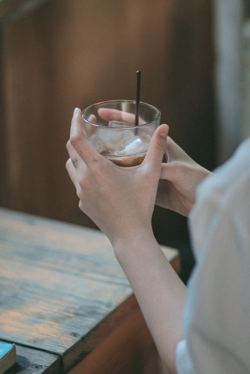 Free A close-up of hands holding an iced drink in a glass with a blurred background, evoking a relaxed mood. Stock Photo