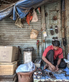 Man working as a street cobbler repairing shoes at a busy market stall.