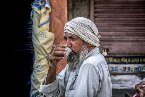 Free Portrait of an elderly man drinking from a cup outdoors in a traditional setting. Stock Photo