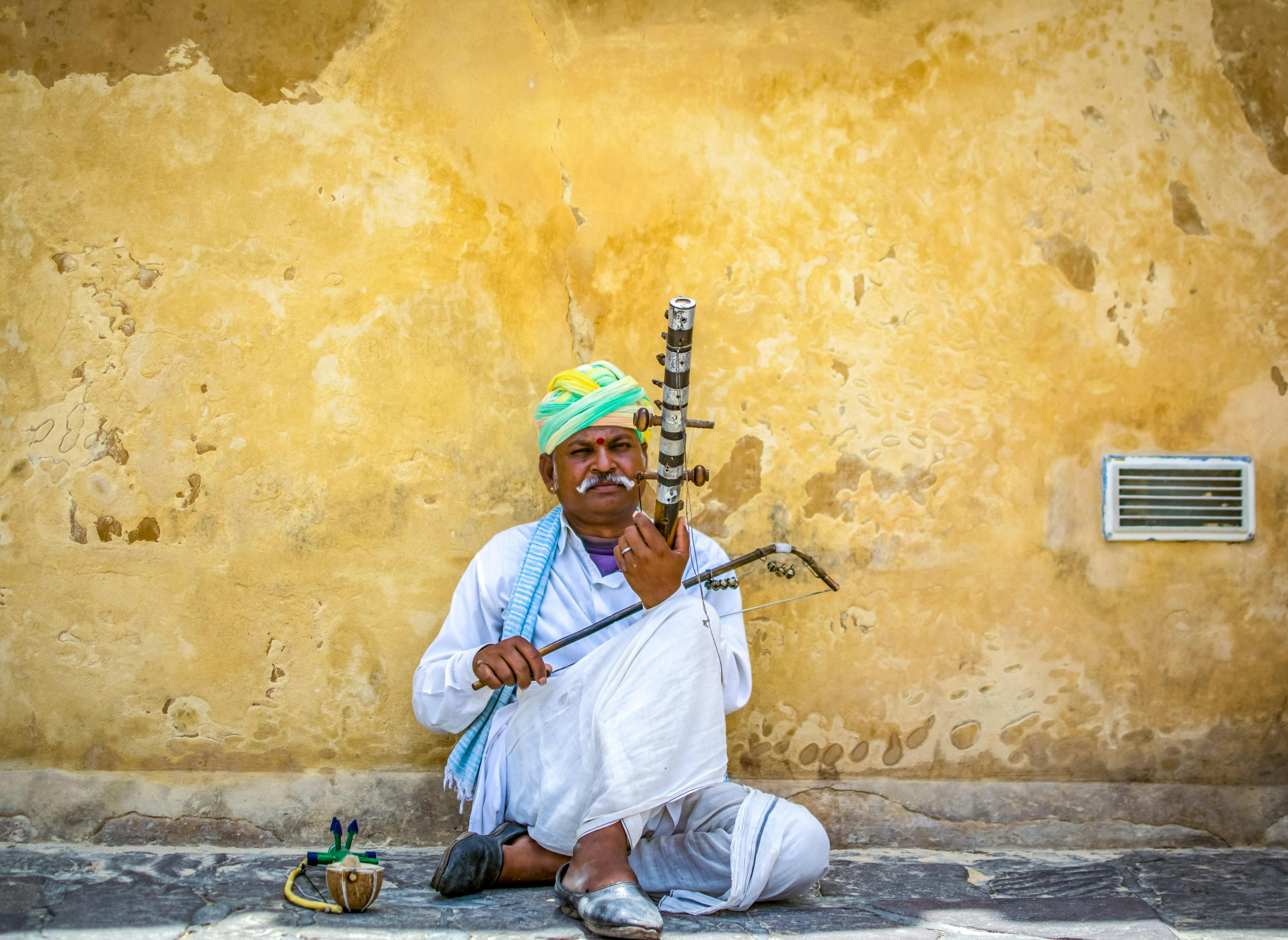 Man Holding String Instrument While Sitting on Concrete Pavement · Free ...
